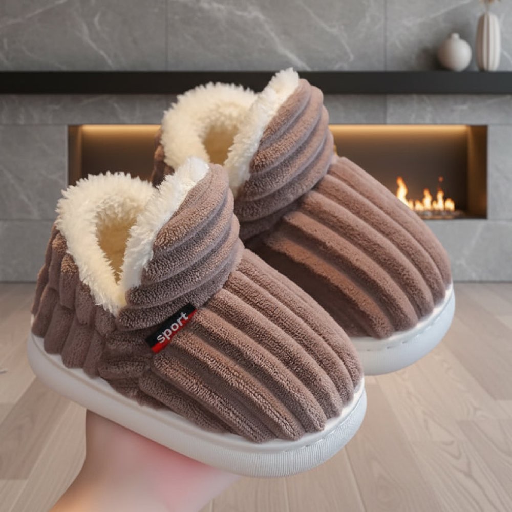 Brown WarmStep winter slippers with a thick plush lining, in front of a fireplace