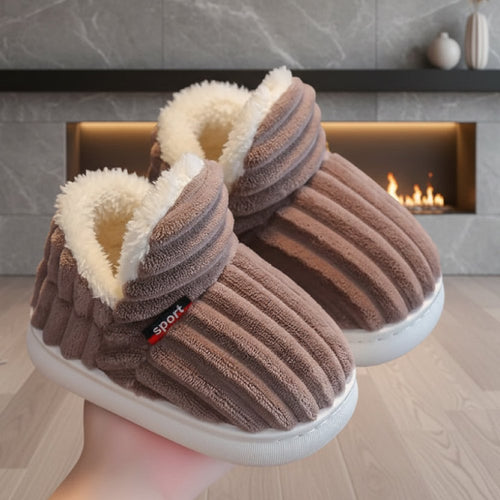 Brown WarmStep winter slippers with a thick plush lining, in front of a fireplace